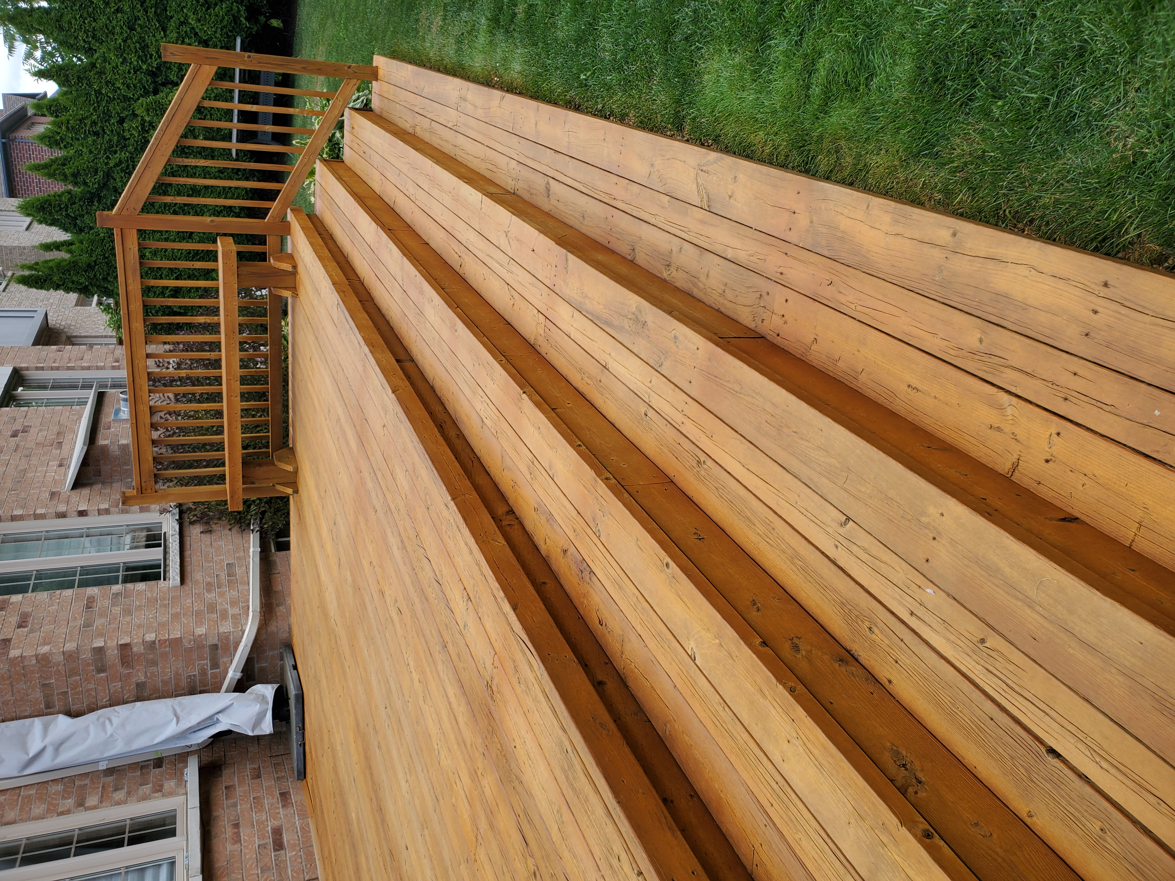 Freshly stained deck with wide full-width stairs — honey gold tone, brick home backdrop