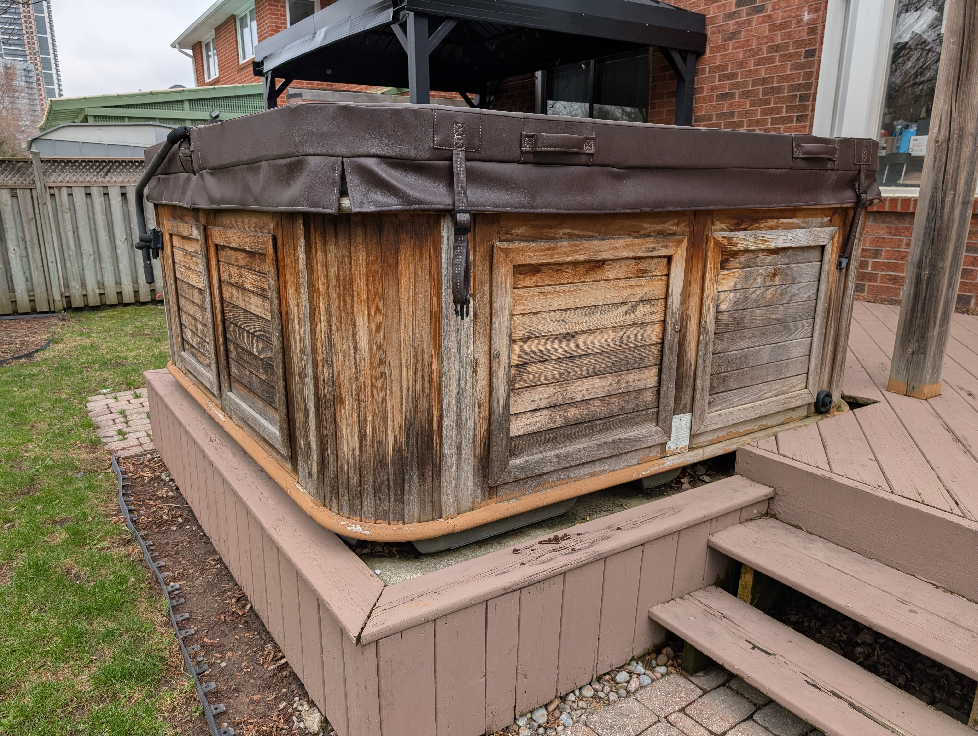 Hot tub surround before — weathered cabinet wood and faded pink painted deck surround