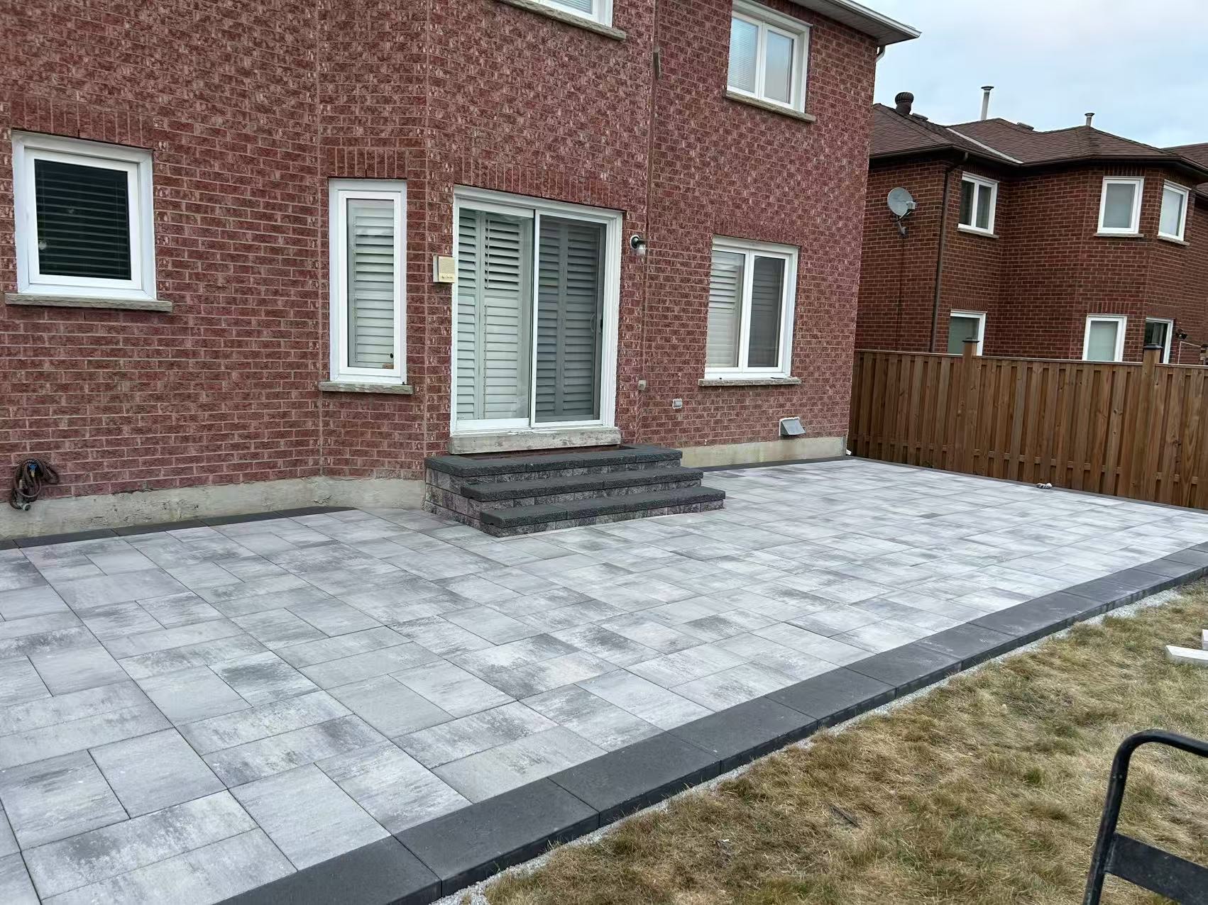 Clean backyard interlock patio with charcoal border and built-in steps
