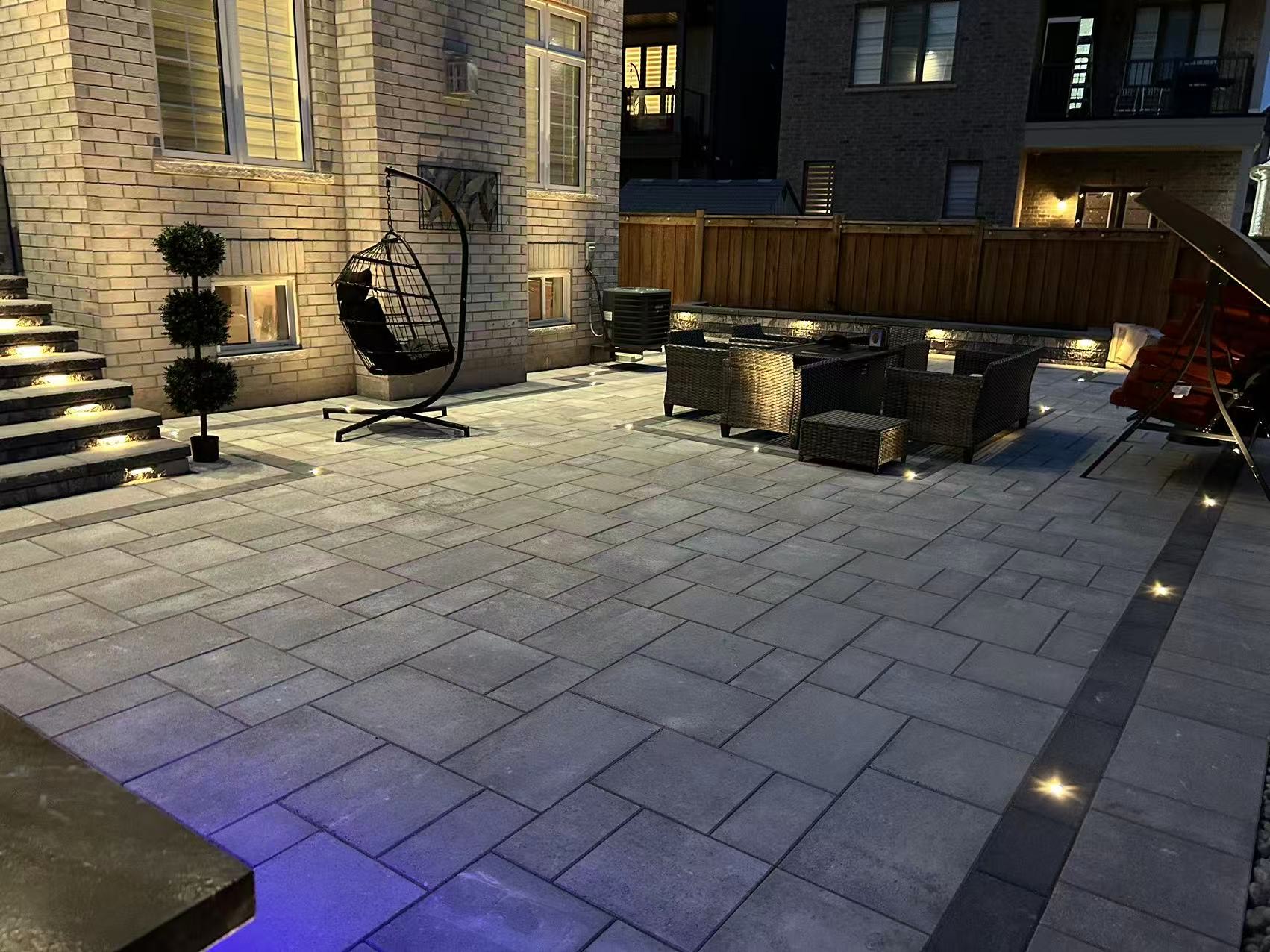 Completed backyard interlock patio at night with ground lighting and outdoor furniture