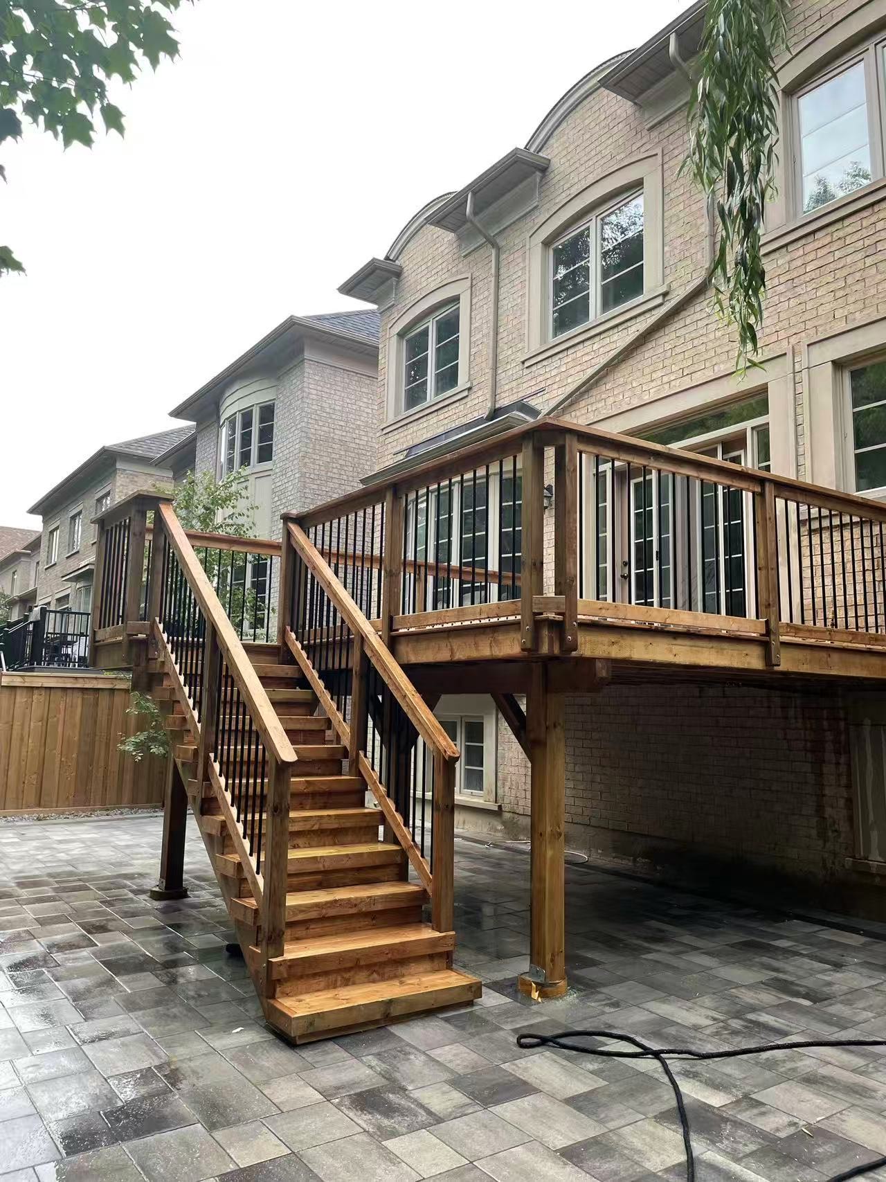Elevated deck with black metal balusters and wood staircase over interlock patio — luxury GTA home