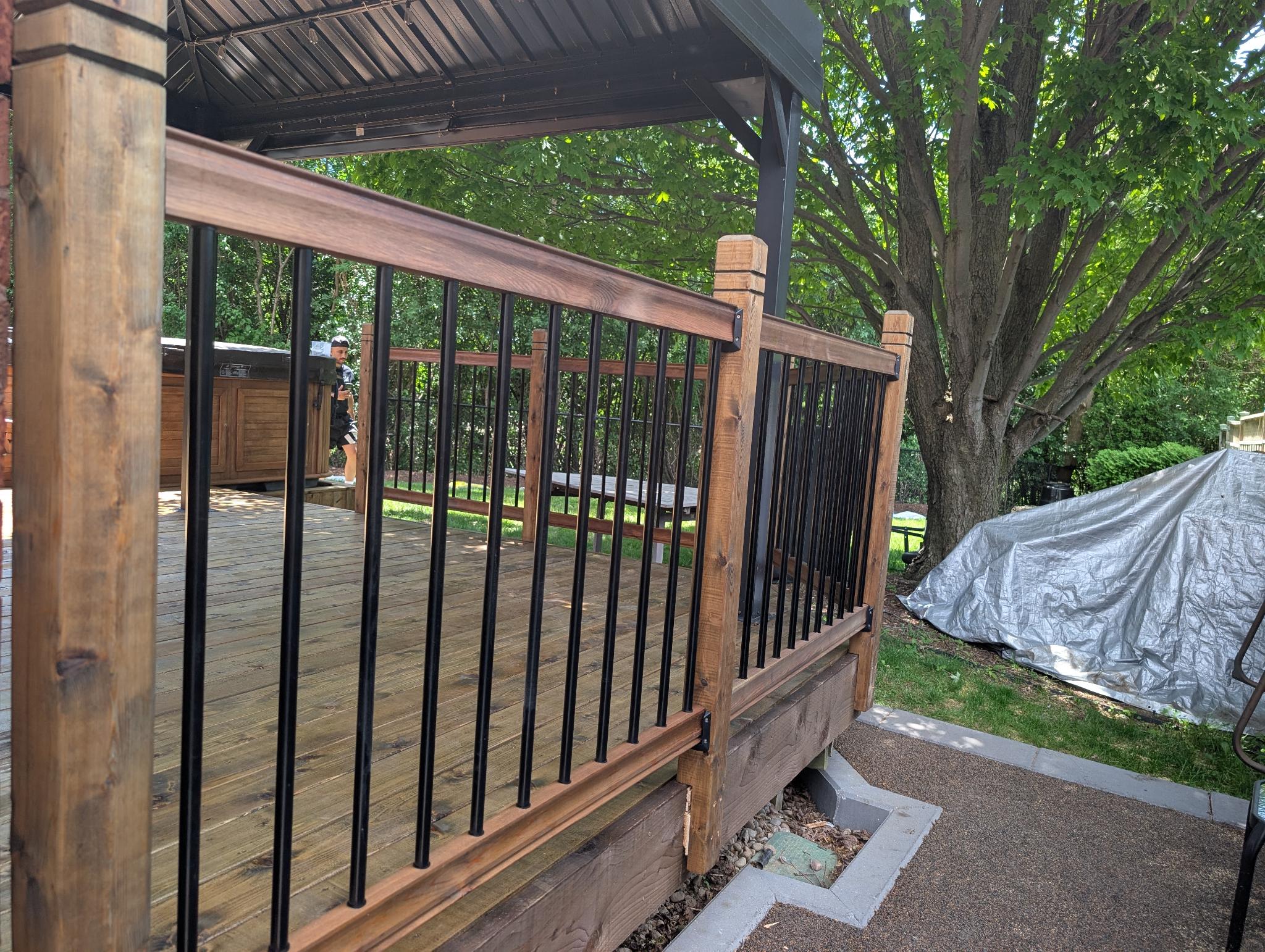 Same gazebo deck after staining — warm brown boards, black balusters, wood posts